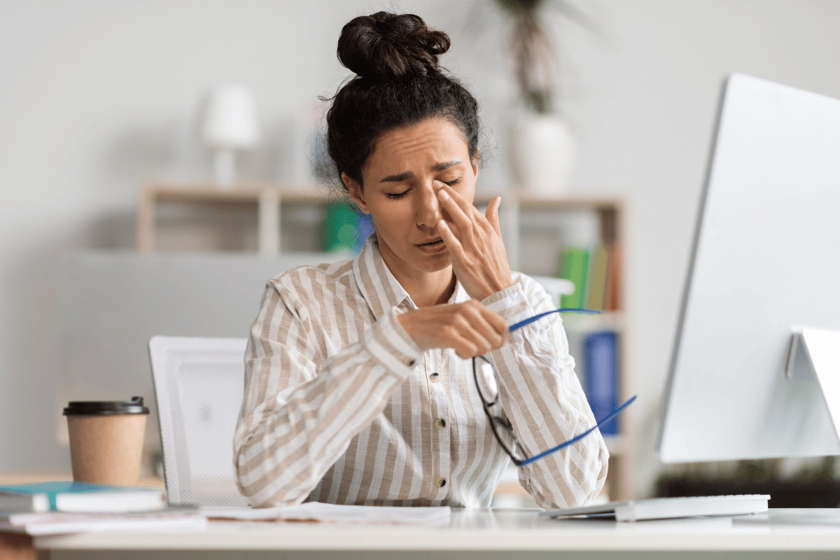 a woman looking uncomfortable and rubbing her face due to dry eye