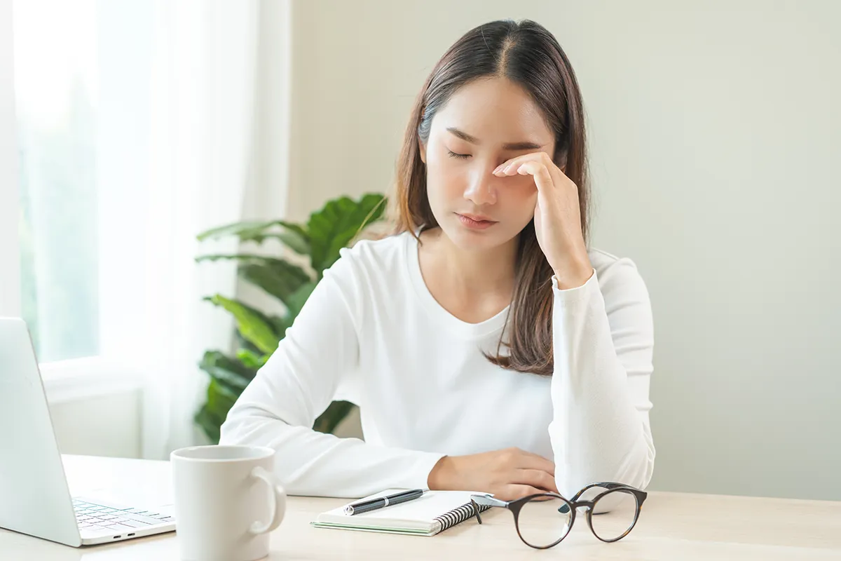 a woman sitting at home and rubbing her eye due to chronic dry eye